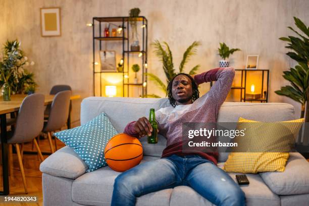 frusterated young man watching a basketball game on a tv at home at night - basketball ball flat stock pictures, royalty-free photos & images