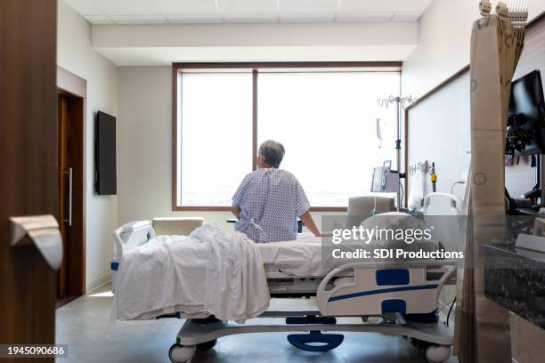 senior adult woman sits alone in her hospital room - old lady in bed stock pictures, royalty-free photos & images