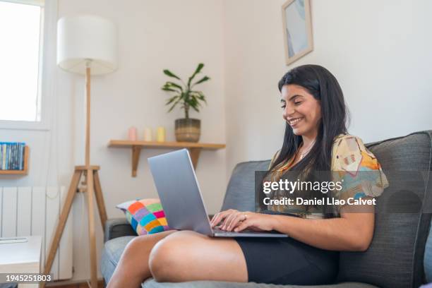 smiling woman using laptop on sofa - casa calvet stock pictures, royalty-free photos & images