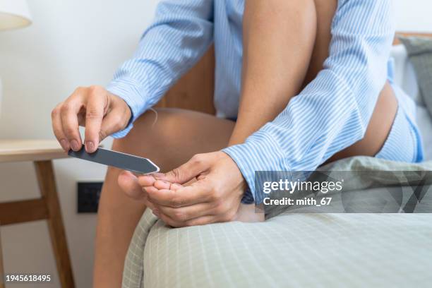 close up shot of unrecognized woman using rasp for filing her toenails after cutting her nails on the bed for body care. female having leisure activity on beauty treatment with wellness. - polishing stock pictures, royalty-free photos & images