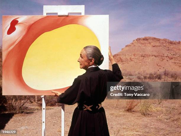 American artist Georgia O'Keeffe stands at an easel outdoors, adjusting a canvas from her 'Pelvis Series- Red With Yellow,' Albuquerque, New Mexico,...