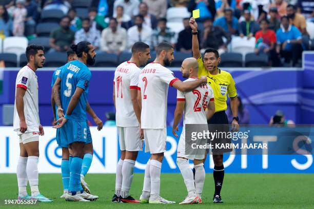 Thai match referee Sivakorn Pu-udom shows a yellow card to Syria's defender Abdul Rahman Weiss during the Qatar 2023 AFC Asian Cup Group B football...