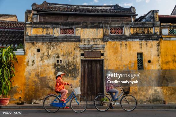 vietnamese women ride bikes in an old town of hoi an city, vietnam - hoi an stockfoto's en -beelden