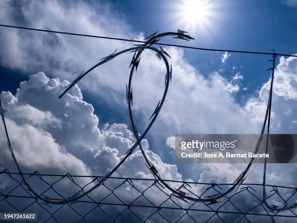 close-up of metal fence with barbed wire over a sunny sky with storm clouds. - border free stock pictures, royalty-free photos & images