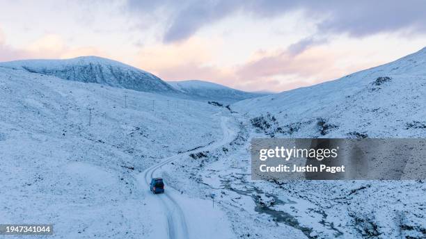 drone/aerial view of a campervan driving on a snow covered road in the scottish highlands - justin van groen stock pictures, royalty-free photos & images