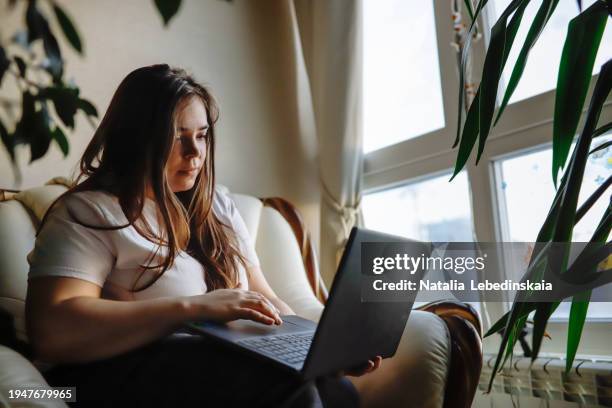 plus-size woman with long hair, embracing laptop at home, copy space - angry typing stock pictures, royalty-free photos & images