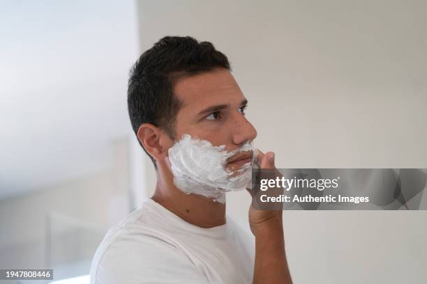 joven aplicando espuma de afeitar en la cara en el baño de su casa - crema de afeitar fotografías e imágenes de stock
