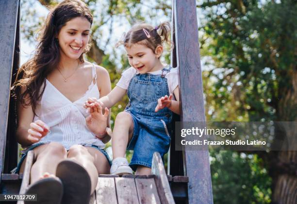 mother and daughter having fun on playground slide outdoors - kindertag stock-fotos und bilder