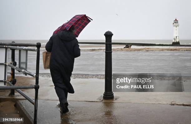 Person struggles with an umbrella in the wind and the rain at the beach at New Brighton in north west England on January 23, 2024. After being hit by...