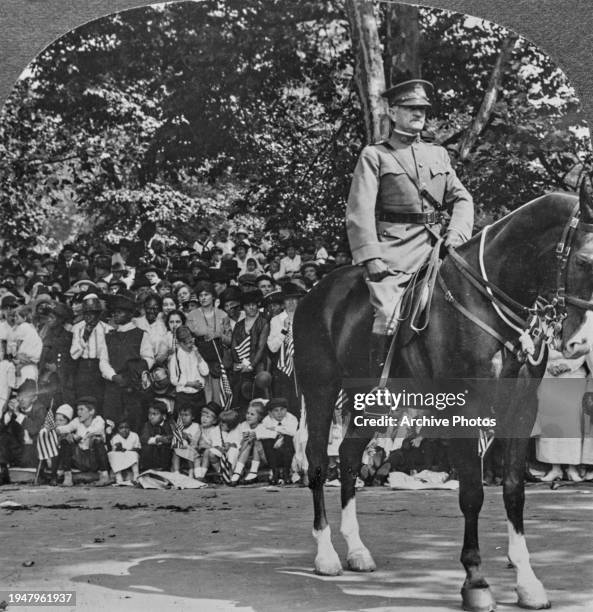 American military officer General John J Pershing on horseback, the horse had been presented as a gift, with a group of onlookers in the background,...