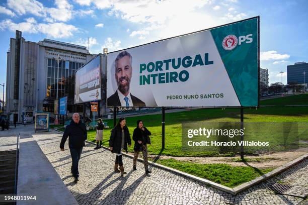 People walk by a Chega! far-right political party billboard campaign poster, showing a portrait of its leader André Ventura, and a Socialist Party...