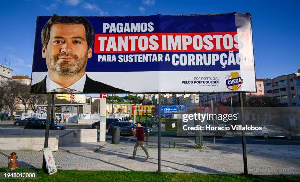 Young man walks behind a Chega! far-right political party billboard campaign poster, showing a portrait of its leader André Ventura, displayed in...