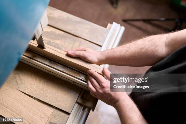 high angle view of a standing carpenter's hands holding wood as he runs it through a saw on his table. - serra-circular imagens e fotografias de stock