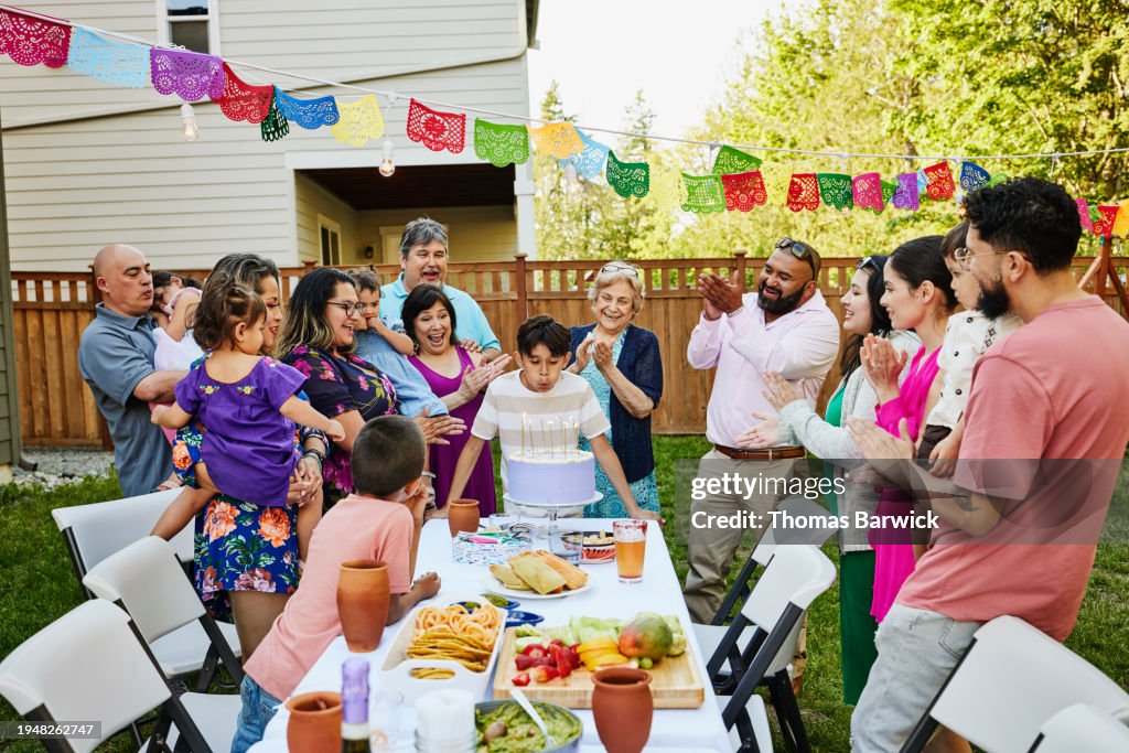 Wide shot boy blowing out candles on cake during summer birthday party