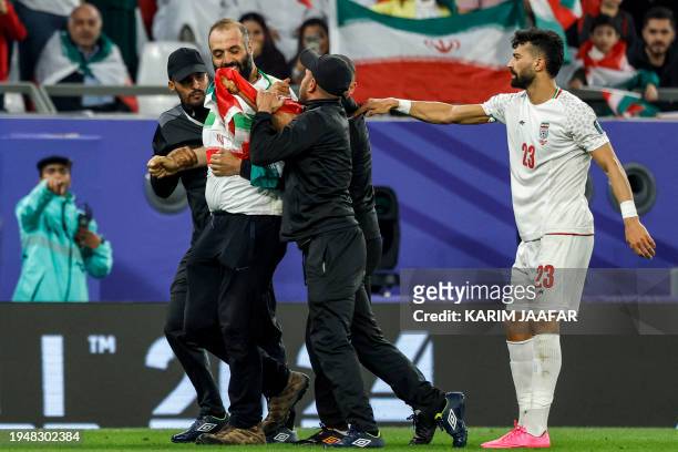 Iran's defender Ramin Rezaeian approaches stadium security as they restrain a pitch invader draped in the Iranian national flag during the Qatar 2023...