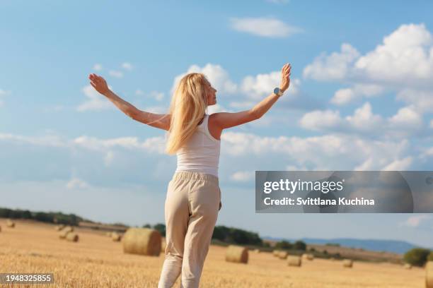 woman running on harvested wheat field with her arms raised - donna meditazione campo di grano foto e immagini stock