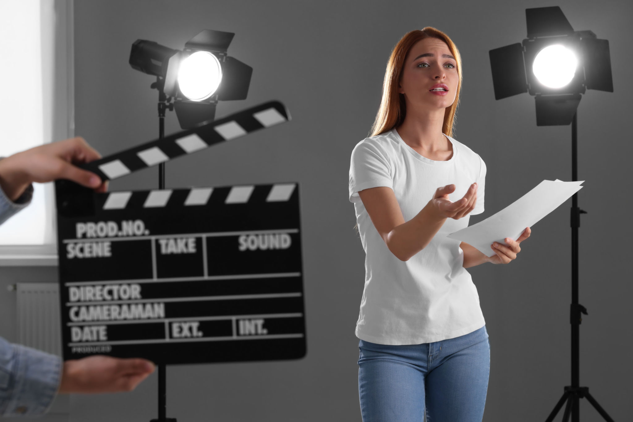 Casting call. Emotional woman performing while second assistance camera holding clapperboard against grey background in studio Casting call. Emotional woman performing while second assistance camera holding clapperboard against grey background in studio
