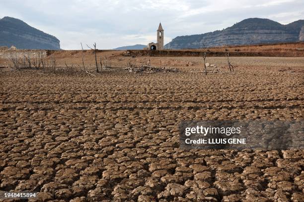 This photograph taken on January 15, 2024 shows the dry soil next to the low water-level reservoir of Sau with in background Sant Roma de Sau church,...
