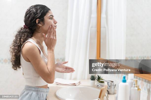 adolescente appliquant de la crème pour le visage dans le miroir - étaler photos et images de collection