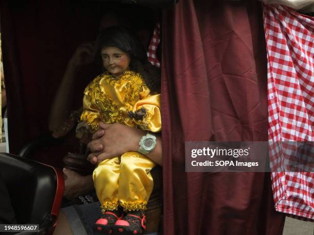 Devotee carries a life-size image of Santo Niño dressed in yellow while inside a passenger electric bike. The Feast of Santo Niño, honoring the Holy...