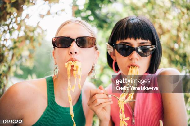 two friends having fun eating italian pasta wearing fancy glasses and accessories - silver spoon in mouth stock pictures, royalty-free photos & images