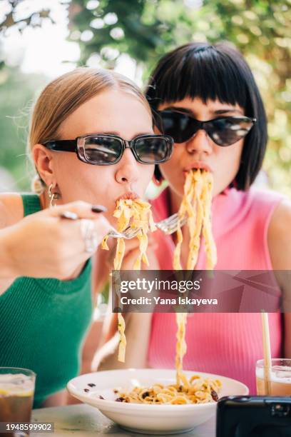 two friends having fun eating italian pasta wearing fancy glasses and accessories - silver spoon in mouth stock pictures, royalty-free photos & images