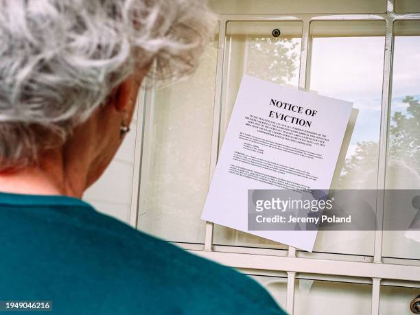 senior woman looking at paper eviction notice on the front door of a home or business - political uncertainty stock pictures, royalty-free photos & images