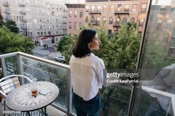 woman looking out the window from her unit in new york - balcony stock pictures, royalty-free photos & images