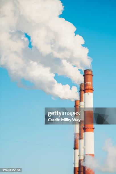 steam and smoke billows from smokestack at massive thermal power plant on blue sky in sunny day. - chimney stock pictures, royalty-free photos & images