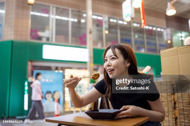 woman eating takoyaki in japanese shopping arcade - takoyaki stock pictures, royalty-free photos & images