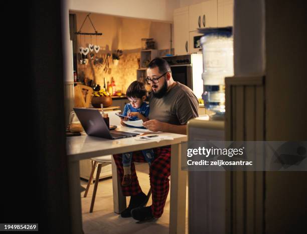 young dad uses laptop and pays bills while son tries to distract him - business finance and industry stock pictures, royalty-free photos & images