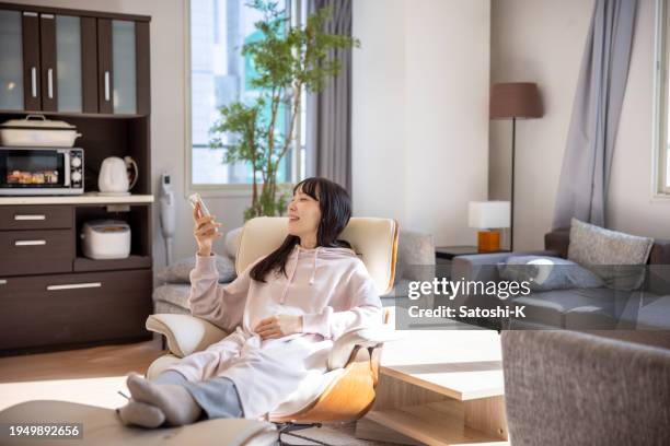 pregnant woman relaxing in living room, using smart phone - asian watching tv stock pictures, royalty-free photos & images