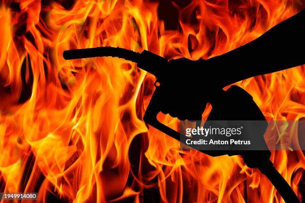 hand holding fuel nozzle on the background of flames - burns stock pictures, royalty-free photos & images