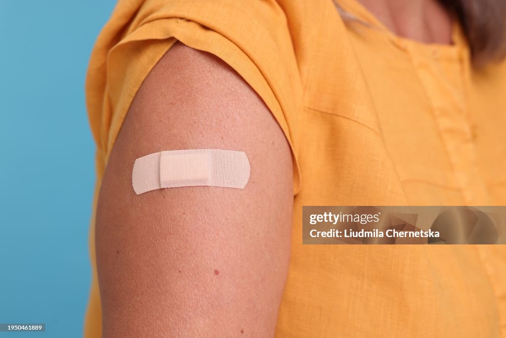 Woman with adhesive bandage on her arm after vaccination against light blue background, closeup