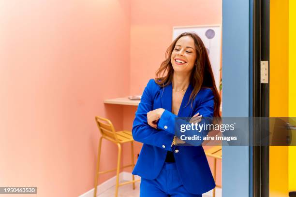 portrait of a beautiful woman standing in the office smiling looking at the camera while smiling crossing her arms, front view - saleswoman stock pictures, royalty-free photos & images