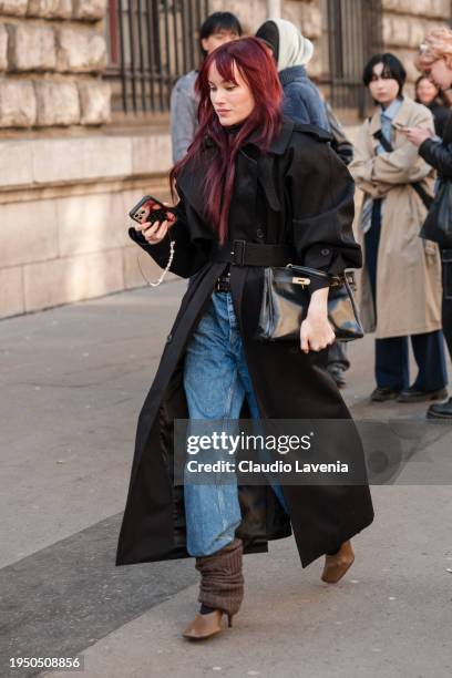 Guest wears a black coat, jeans, black bag, brown leg warmers, brown heels, outside Loewe, during the Menswear Fall/Winter 2024/2025 as part of Paris...