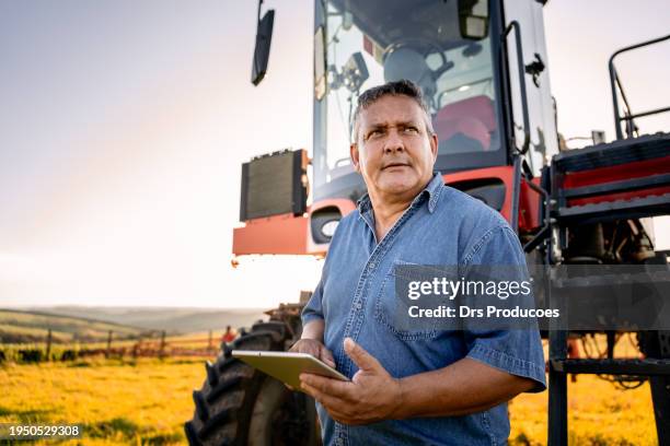 retrato de un agrónomo con una tableta frente a la máquina agrícola - equipos agrícolas fotografías e imágenes de stock