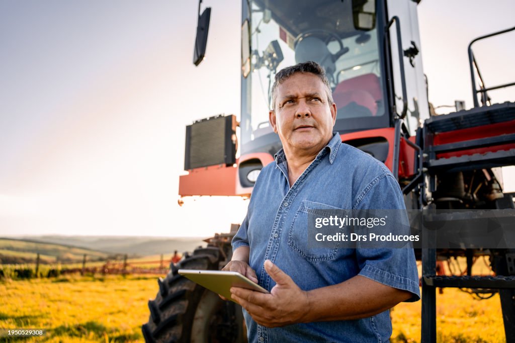Portrait of an agronomist with a tablet in front of the agricultural machine
