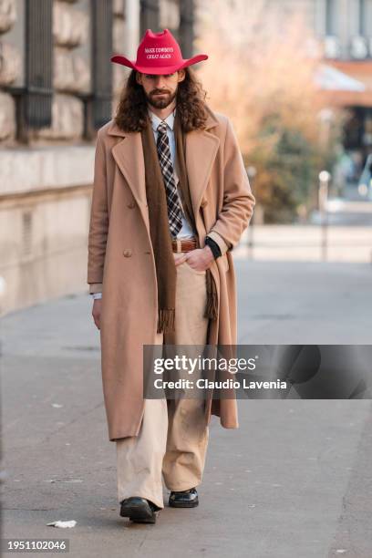 Guest wears red hat, white shirt, checked tie, brown scarf, camel coat, beige pants, outside Loewe, during the Menswear Fall/Winter 2024/2025 as part...