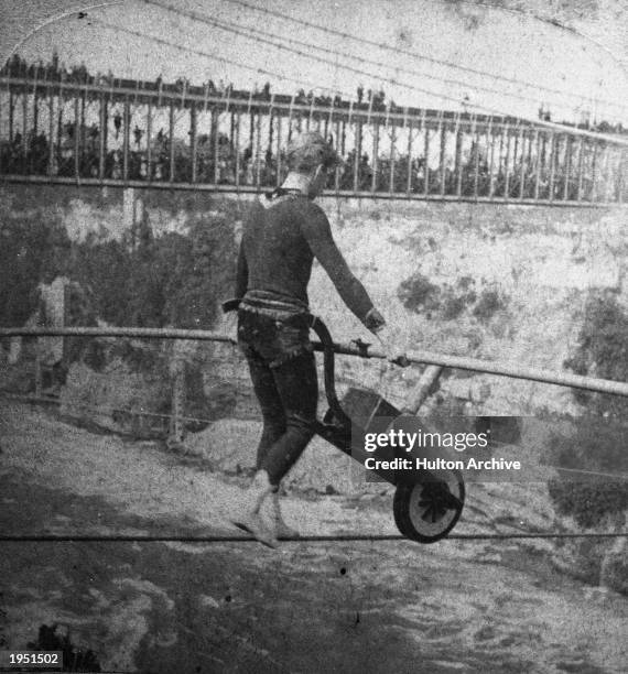 French daredevil Jean Francois Gravelet Blondin, a.k.a 'The Great Blondin,' pushes a wheelbarrow while tightrope walking across the Niagara River...