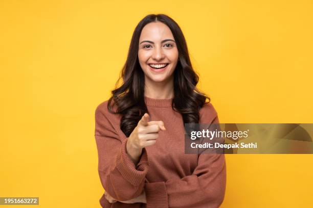 photo of young women in winter wear standing on yellow background stock photo - hand pointing at camera stock pictures, royalty-free photos & images