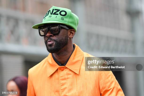 Guest wears a green Kenzo hat, a neon orange long trench coat, outside Sacai, during the Menswear Fall/Winter 2024/2025 as part of Paris Fashion Week...