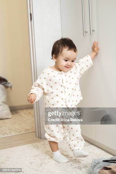 cute baby toddler is holding on to the wall, the first steps. - baby first steps stock pictures, royalty-free photos & images