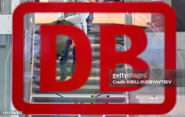 The logo of German railway operator Deutsche Bahn is seen on a window as a train passenger carries her suitcase down the stairs at the main railway...