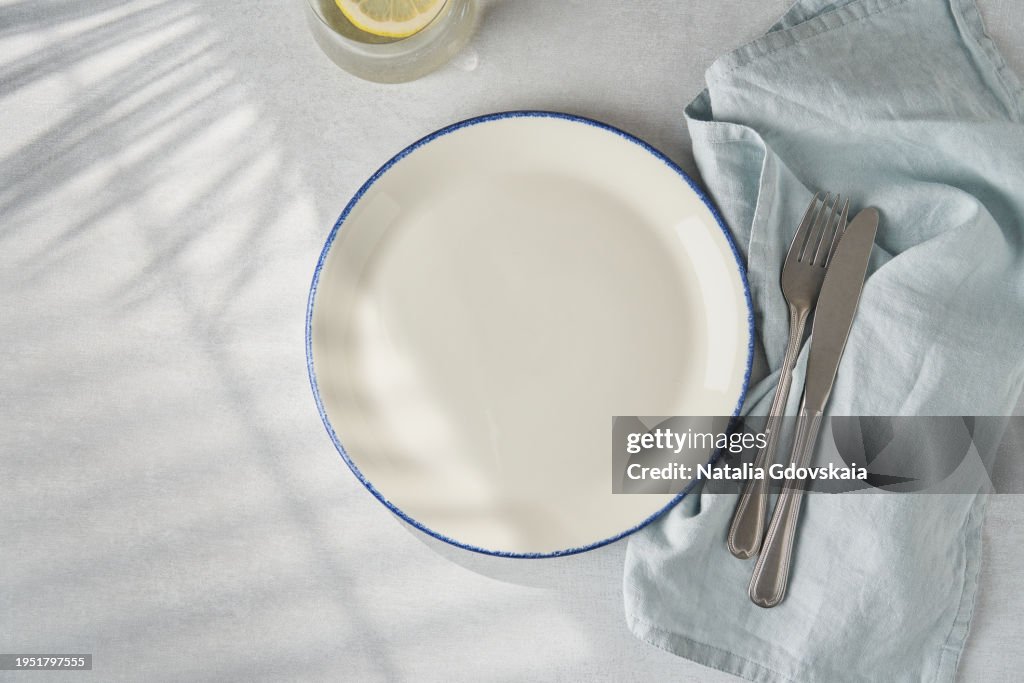 Clean empty white plate, fork and knife on pastel grey table. Concept for menu with utensil