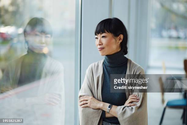 sonriente mujer de negocios japonesa soñando despierta junto a la ventana. - woman day dreaming fotografías e imágenes de stock
