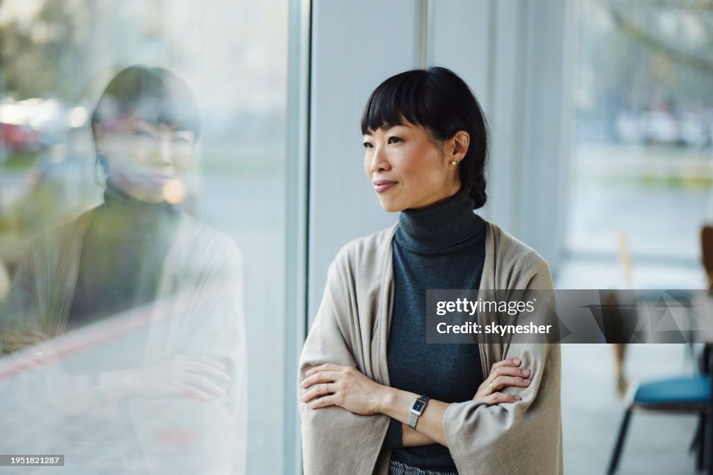 Smiling Japanese businesswoman day dreaming by the window.