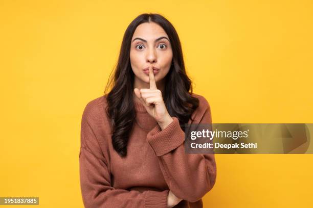 photo of young women in winter wear standing on yellow background stock photo - finger on lips stock pictures, royalty-free photos & images