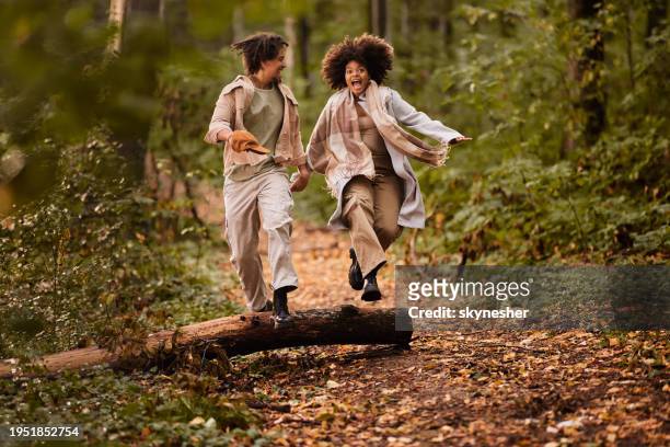 cheerful black couple jumping over tree trunk in autumn day. - wood stock pictures, royalty-free photos & images