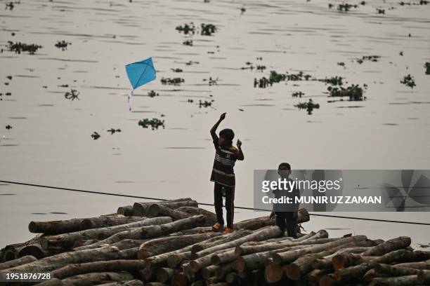 Children fly a kite atop a pile of wood logs on the banks of the Buriganga River in Dhaka on January 25, 2024.